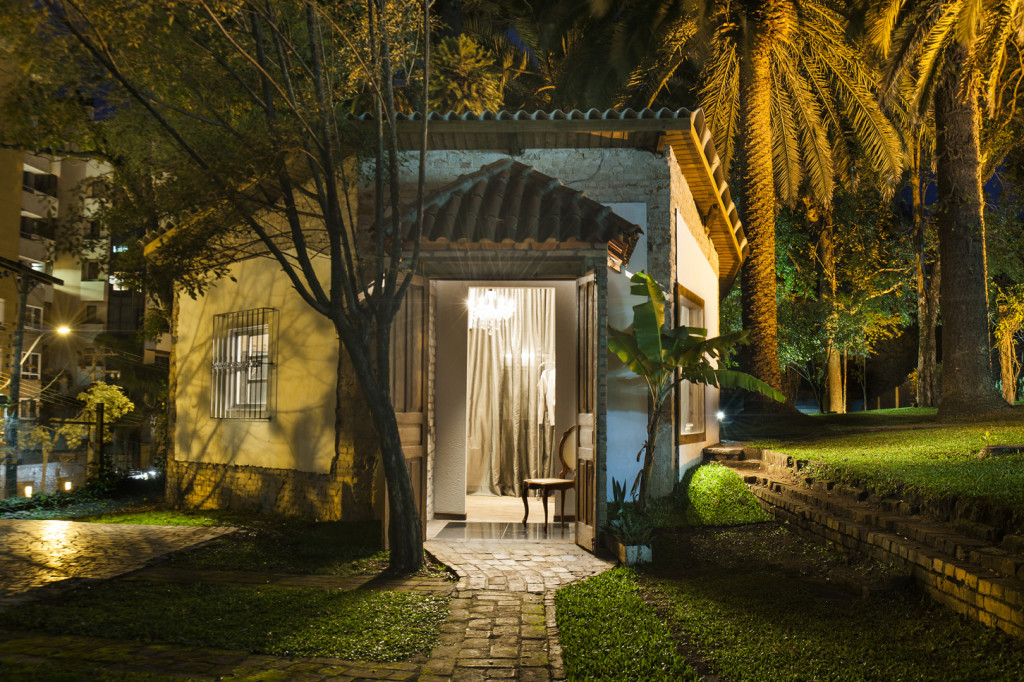 Desde a fachada, o elegante atelier inspira aconchego. O verde à sua volta, as telhas de barro, os tijolos aparentes pintados na cor branca e o gracioso hall com lustre clássico exercem um poderoso atrativo