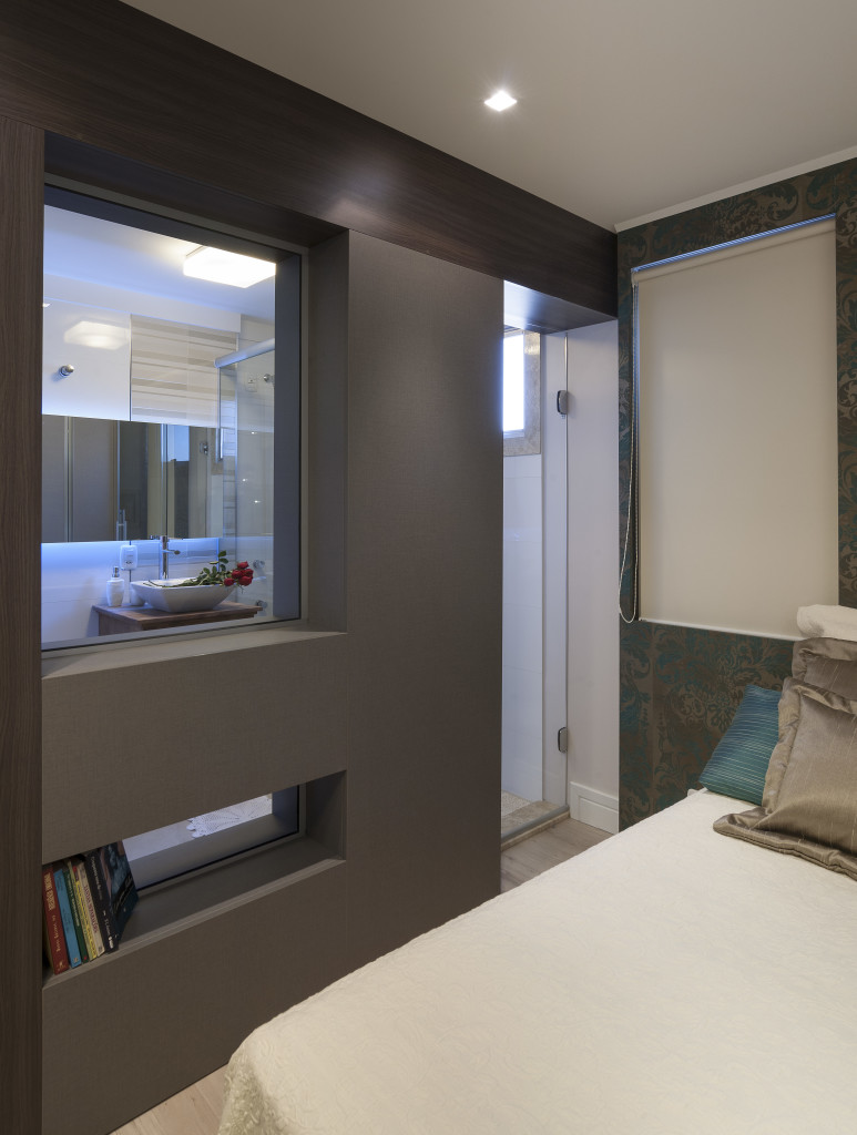 Imagem da integração entre o quarto e o banheiro, feita por meio de uma parede com abertura de vidro.